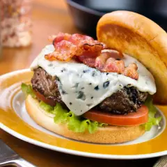 Un délicieux burger avec un fromage à burger fondant, du bacon croustillant, de la laitue et de la tomate, servi sur une assiette jaune.