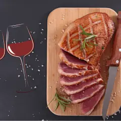 Un canard rôti tranché sur une planche en bois, accompagné de deux verres de vin rouge. La question se pose : quel vin avec le canard pour un repas parfait ?