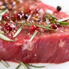 Un morceau de bœuf cru, assaisonné de poivre rose, de romarin et d'épices, promettant le meilleur bœuf du monde.
