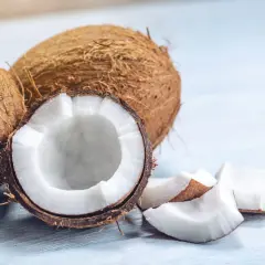 Noix de coco entières et coupées, révélant leur chair blanche et leur peau fibreuse. Des morceaux de noix de coco sont dispersés autour.