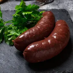 Deux boudins rouges antillais, brillants et appétissants, accompagnés de persil frais sur une ardoise sombre.