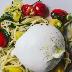 Un plat de pâtes avec une burrata crémeuse, des tomates cerises rouges et jaunes, et des herbes vertes.