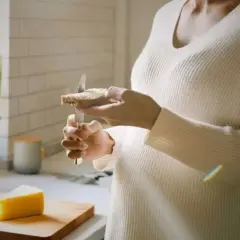 Une personne tartine une tranche de pain avec du fromage au lait cru. Un morceau de fromage est posé sur une planche à découper.