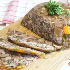 Tranche de fromage de tête, un plat traditionnel à base de viande et de légumes en gelée, garni de persil frais.