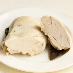 Un morceau de poulet poché dans un bouillon savoureux, coupé en deux pour montrer sa tendreté. Accompagné de feuilles de laurier.