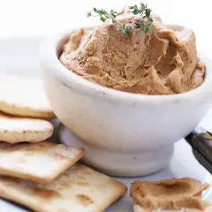 Un bol de pâté onctueux, garni de thym, servi avec des crackers. Un débat culinaire : foie gras vs pâté.