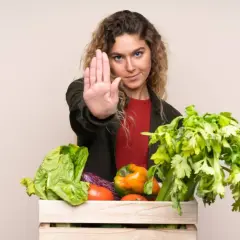Femme faisant un geste d'arrêt devant une caisse de légumes frais, comme pour dire non aux légumes crus toxiques.