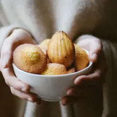 Mains tenant un bol de madeleines dorées, évoquant la madeleine de Proust recette.