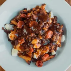 Une assiette généreuse de recette poutine québécoise, avec frites, fromage en grains, sauce brune et morceaux de saucisses.
