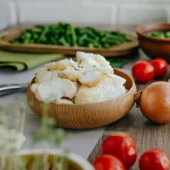 Un bol en bois rempli de champignon criniere de lion, prêt pour une recette savoureuse. Tomates, oignon et herbes l'accompagnent.