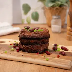 Trois galettes de haricot rouge empilées, garnies de haricots rouges et de ciboule. Épices et haricots rouges parsèment la planche à découper.