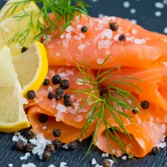 Une présentation de Noël : fines tranches de saumon fumé, parsemées de gros sel et de poivre, avec des quartiers de citron et de l'aneth.