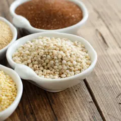Quatre bols de céramiques blanches présentent diverses céréales sans gluten : millet, sorgho, quinoa et amarante.