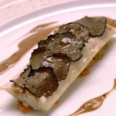 Un plat de poisson délicat, garni de fines lamelles de truffe de la Saint-Jean, arrosé d'une sauce onctueuse sur une assiette blanche.