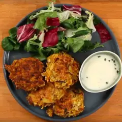 Trois croquettes de légumes dorées, accompagnées d'une salade fraîche et d'une sauce crémeuse.