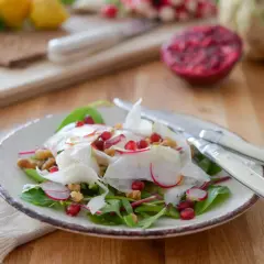 Salade croquante de céleri rave, radis, grenade et noix, garnie de feuilles vertes. Un délice frais et coloré.