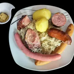 Assiette de choucroute garnie avec pommes de terre, saucisses et viandes, un petit ramequin de moutarde à côté. Un plat riche en saveurs et en vitamine C !