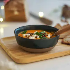 Un bol de soupe butternut tomate onctueuse, garnie de fromage frais et de noix, servi avec du pain grillé.
