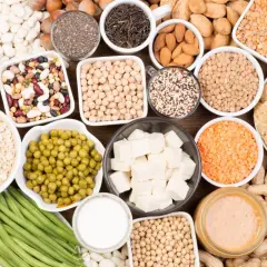 Un assortiment de bols et d'assiettes remplis d'aliments riches en protéines végétales : lentilles, pois chiches, haricots, tofu, noix, graines, avoine, edamame, beurre de cacahuète.
