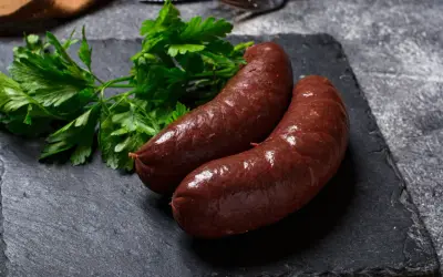 Deux boudins rouges antillais, brillants et appétissants, accompagnés de persil frais sur une ardoise sombre.