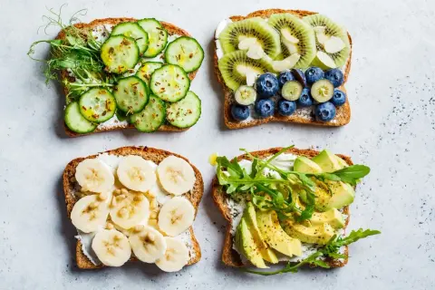 Quatre tartines garnies : concombre et pousses, kiwi et myrtilles, banane et pignons, avocat et roquette. Un régal pour un goûter sain.