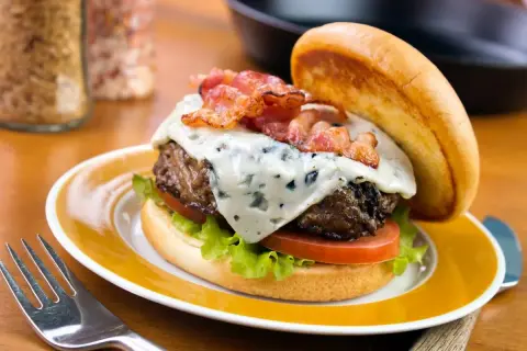 Un délicieux burger avec un fromage à burger fondant, du bacon croustillant, de la laitue et de la tomate, servi sur une assiette jaune.