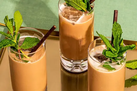 Trois mocktails rafraîchissants à la menthe et au chocolat, servis dans des verres hauts avec de la glace et des pailles foncées.