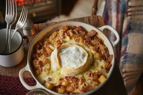Un plat de tartiflette fumant, avec son fromage fondant au centre. Qui a inventé la tartiflette ? Ce plat savoyard réconfortant.