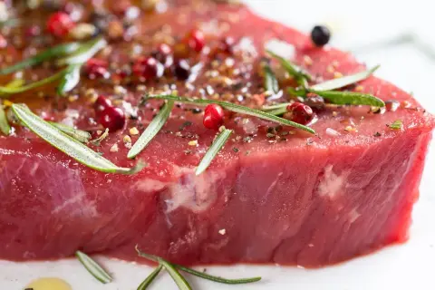 Un morceau de bœuf cru, assaisonné de poivre rose, de romarin et d'épices, promettant le meilleur bœuf du monde.