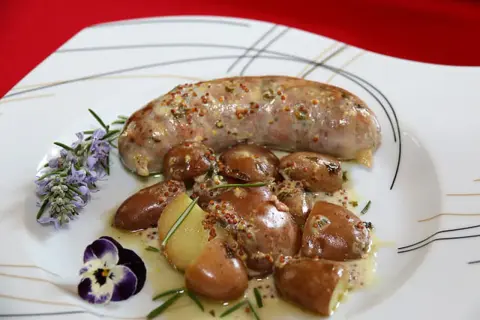 Une andouillette sauce moutarde, accompagnée de pommes de terre grenaille et d'une touche de romarin et de pensée.