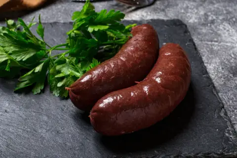 Deux boudins rouges antillais, brillants et appétissants, accompagnés de persil frais sur une ardoise sombre.