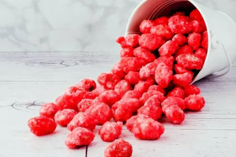 Un seau blanc renversé déverse des bonbons roses brillants, parfaits pour une recette praline rose.