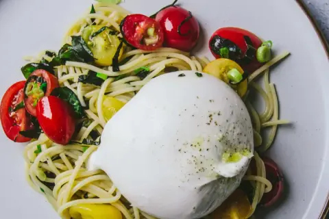 Un plat de pâtes avec une burrata crémeuse, des tomates cerises rouges et jaunes, et des herbes vertes.
