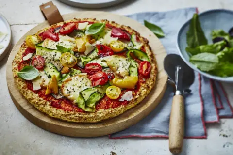 Délicieuse pizza aux légumes frais et fromage, sur une pâte sans gluten, servie sur une planche en bois.