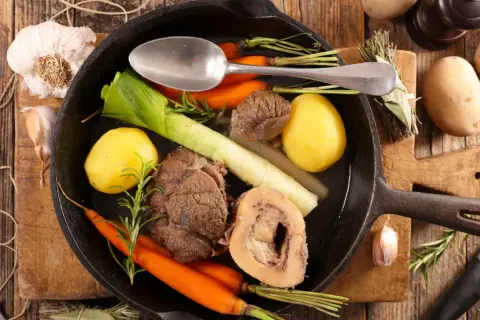 Un pot au feu savoureux, digne d'un journal des femmes, mijote dans une poêle en fonte avec des légumes et de la viande.