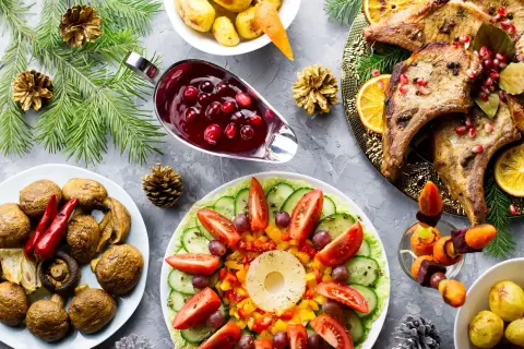 Une table dressée pour une entrée chaude festive : côtelettes de porc, légumes rôtis, salade colorée et sauce aux airelles.