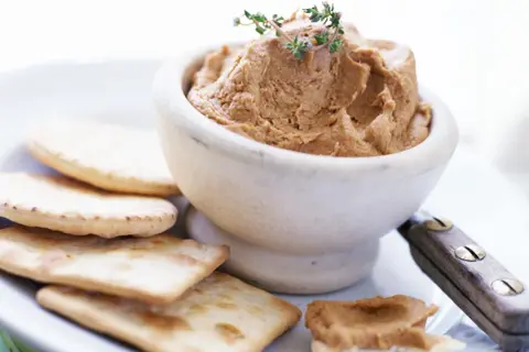 Un bol de pâté onctueux, garni de thym, servi avec des crackers. Un débat culinaire : foie gras vs pâté.