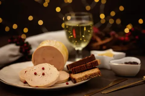 Foie gras maison servi avec du pain d'épices et une coupe de vin blanc. Quel alcool pour foie gras maison ? Un vin doux naturel ou un Sauternes serait parfait.