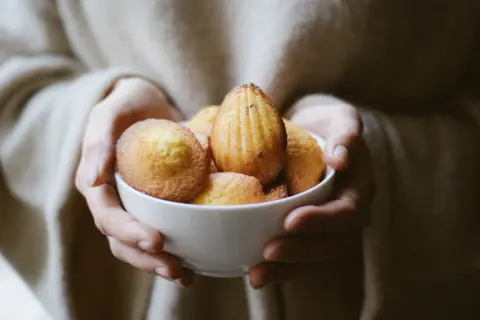 Mains tenant un bol de madeleines dorées, évoquant la madeleine de Proust recette.