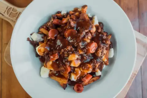 Une assiette généreuse de recette poutine québécoise, avec frites, fromage en grains, sauce brune et morceaux de saucisses.