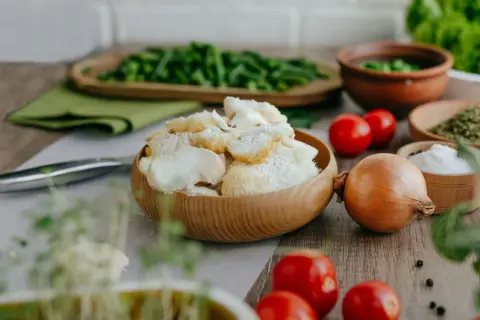 Un bol en bois rempli de champignon criniere de lion, prêt pour une recette savoureuse. Tomates, oignon et herbes l'accompagnent.