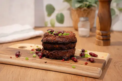 Trois galettes de haricot rouge empilées, garnies de haricots rouges et de ciboule. Épices et haricots rouges parsèment la planche à découper.
