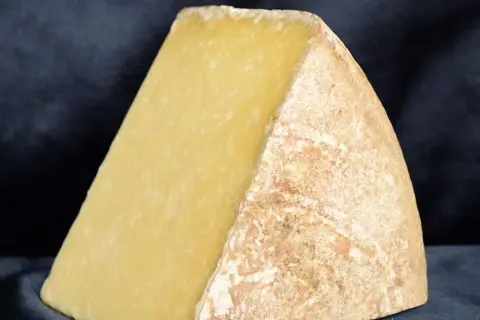 Gros morceau de fromage à pâte dure, jaune pâle, avec une croûte naturelle. Parfait pour la fondue ou un plateau de fromage de Noël.
