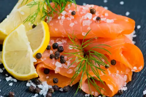 Une présentation de Noël : fines tranches de saumon fumé, parsemées de gros sel et de poivre, avec des quartiers de citron et de l'aneth.