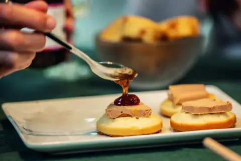 Une cuillère verse une touche de confiture sur un toast original de foie gras. Délicieux !