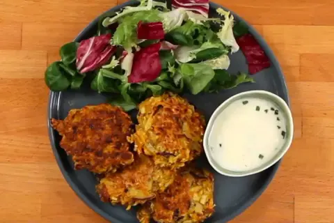 Trois croquettes de légumes dorées, accompagnées d'une salade fraîche et d'une sauce crémeuse.