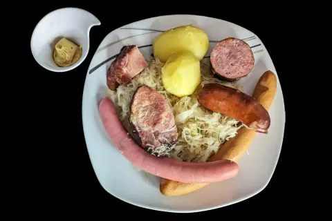 Assiette de choucroute garnie avec pommes de terre, saucisses et viandes, un petit ramequin de moutarde à côté. Un plat riche en saveurs et en vitamine C !