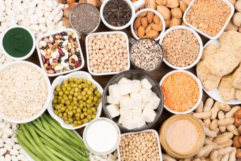 Un assortiment de bols et d'assiettes remplis d'aliments riches en protéines végétales : lentilles, pois chiches, haricots, tofu, noix, graines, avoine, edamame, beurre de cacahuète.