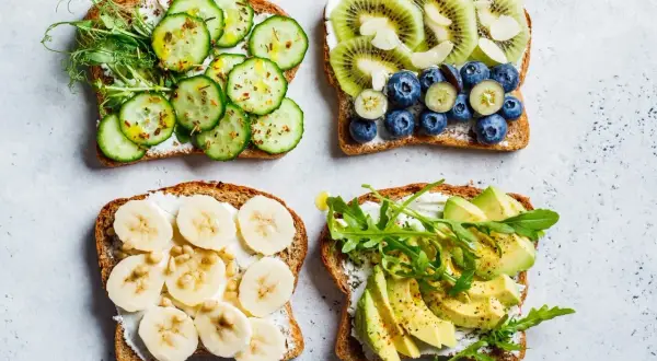 Quatre tartines garnies : concombre et pousses, kiwi et myrtilles, banane et pignons, avocat et roquette. Un régal pour un goûter sain.