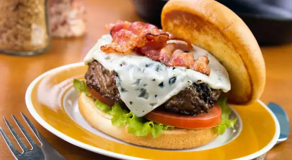 Un délicieux burger avec un fromage à burger fondant, du bacon croustillant, de la laitue et de la tomate, servi sur une assiette jaune.